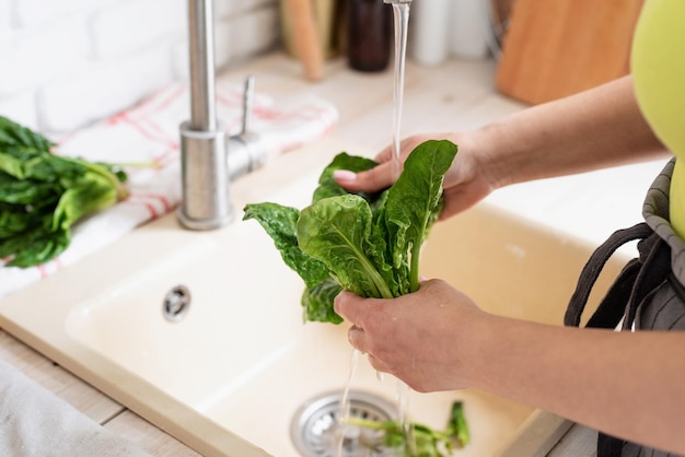 Preparazione di cibi sani Alimentazione sana e dieta Giovane donna sorridente in abiti domestici che lava gli spinaci in cucina