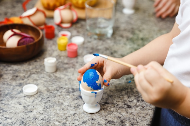 Preparazione di Pasqua del capretto dipingendo le uova di Pasqua e le decorazioni di festa a casa del primo piano