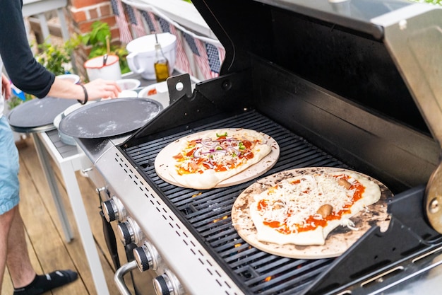 Preparazione di singole pizze alla griglia su una griglia a gas all'aperto.