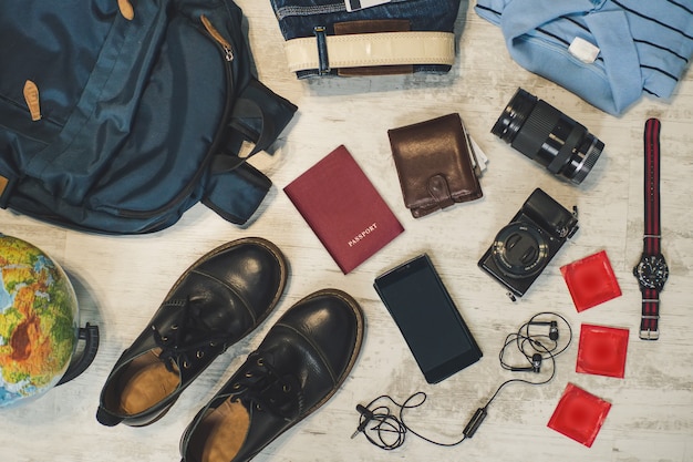 Preparazione per il concetto di attività di viaggio all'aperto, piatto. zaino passaporti, portafoglio, telefono e valute, camicia, macchina fotografica, passaporto, preservativi telefonici e altri accessori da viaggio raccolti su pavimento in legno