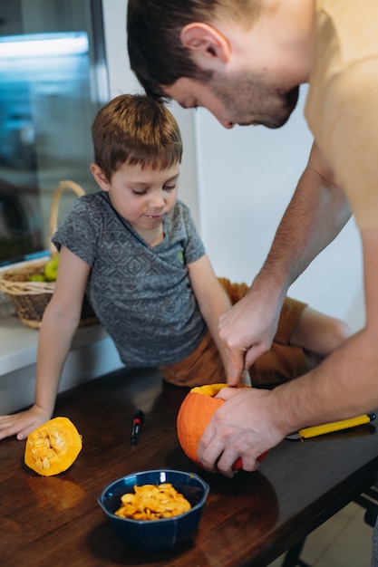 Preparazione per la celebrazione di halloween. Uomo caucasico con il suo simpatico figlio di 6 anni che disegna gli occhi su una zucca per realizzare la tradizionale lanterna Jack. Immagine con messa a fuoco selettiva. Foto di alta qualità