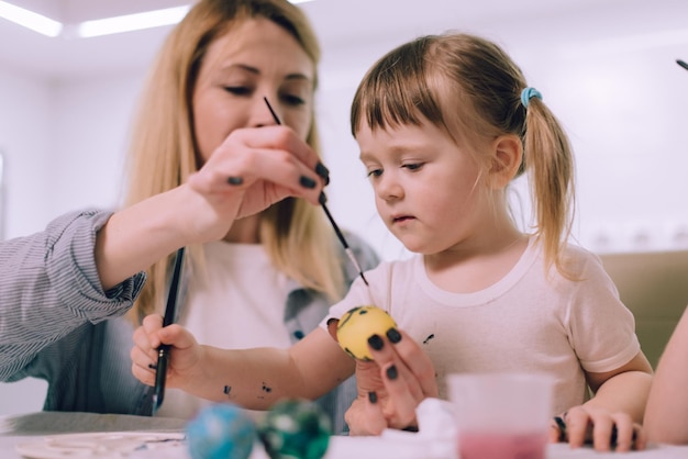 Preparazione per la Pasqua Una bambina sta dipingendo le uova con la sua famiglia in cucina a casa Primo piano