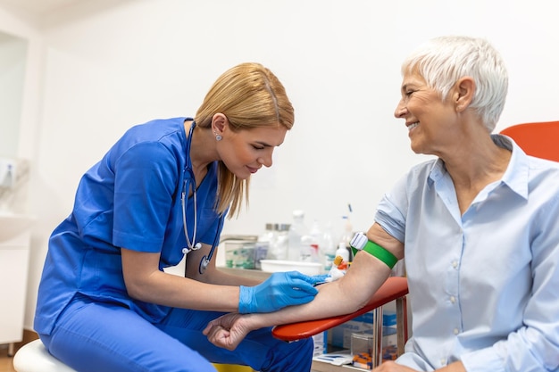 Preparazione per un esame del sangue con una donna anziana da parte di una dottoressa uniforme medica sul tavolo in una stanza bianca e luminosa L'infermiera trafigge la vena del braccio del paziente con un tubo vuoto con l'ago