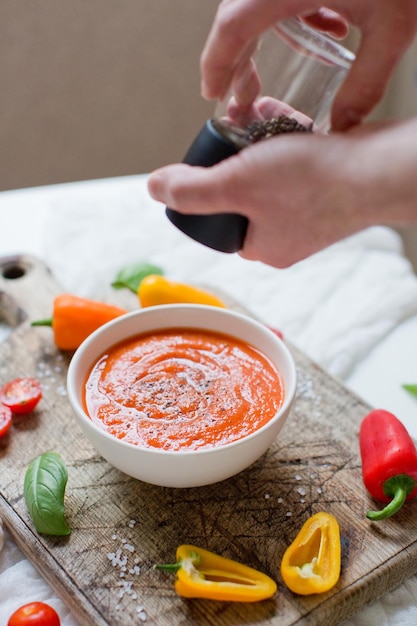 Preparazione zuppa di pomodoro rosso vegetale con pomodori peperoni aglio e basilico L'uomo aggiunge pepe nero piccante dallo shaker