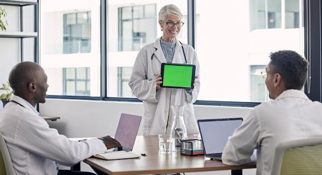 Presentazione del tablet con schermo verde e riunione dei medici per i risultati della ricerca ospedaliera e la soluzione clinica software Spazio mockup professionale medico e successo della donna anziana con le persone interessate