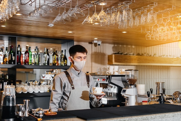 Presentazione di un barista in una maschera di delizioso caffè biologico in un moderno caffè durante la pandemia