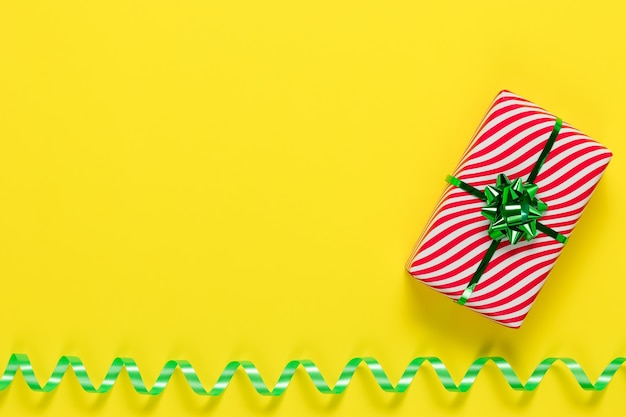 Presente, confezione regalo a strisce avvolto con fiocco verde su sfondo di carta gialla.