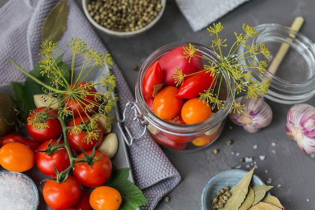 Preservare pomodori freschi e sottaceto, condimenti e aglio su un tavolo di cemento grigio