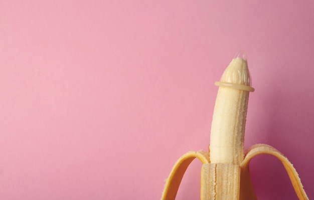 Preservativo e banana su sfondo rosa con spazio di copia