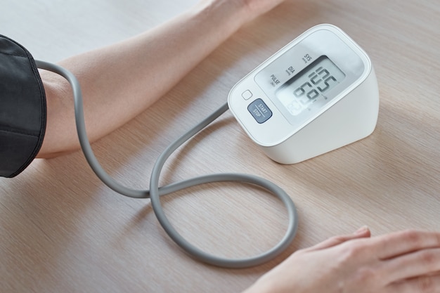 Pressione sanguigna di misurazione della donna con il monitor di pressione digitale contro fondo blu. Concetto di assistenza sanitaria e medica