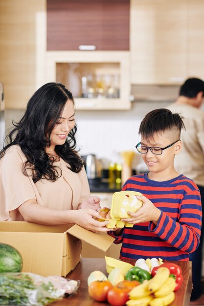 Preteen ragazzo vietnamita che aiuta la madre a prendere la spesa dalla scatola di cartone