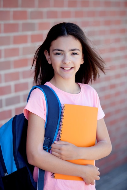 Preteenager ragazza accanto a un muro di mattoni rossi con lo zaino e libri