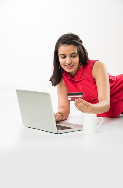 Pretty Indian Asian Girl shopping online utilizzando carta di credito o di debito sul computer portatile, su sfondo bianco