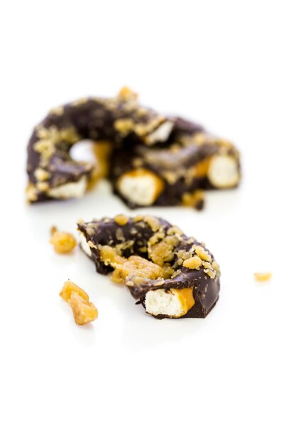 Pretzel ricoperto di cioccolato gourmet con arachidi candite su sfondo bianco.