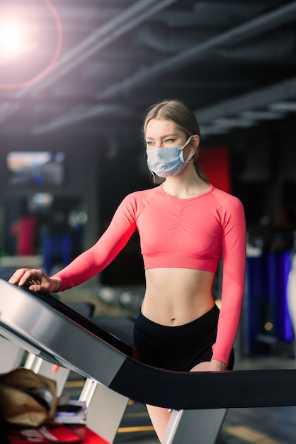 Prevenzione del coronavirus covid-19, ragazza fitness con una maschera medica in posa in palestra. Combattere i virus.