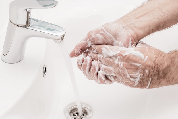 Prevenzione del coronavirus lavarsi le mani con sapone antibatterico all'igiene delle mani dell'uomo del lavandino del bagno.