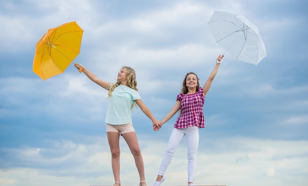 Previsioni meteo Cambiamenti meteorologici Bambini spensierati all'aperto Ventoso o piovoso siamo preparati Libertà e freschezza Pronti per qualsiasi tempo Ragazze amiche con ombrelloni sfondo con cielo nuvoloso