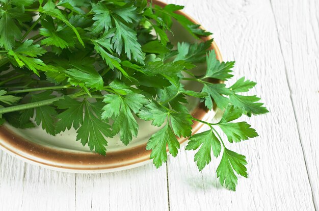 Prezzemolo verde fresco in piatto sulla tavola bianca di legno