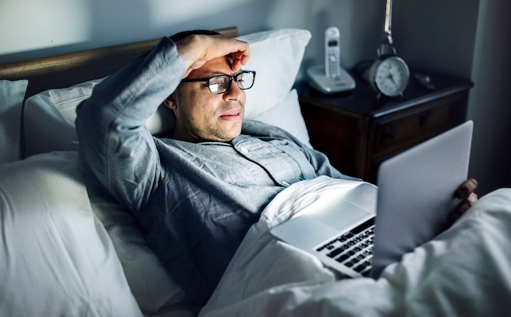 Photo pria menggunakan laptop di tempat tidur