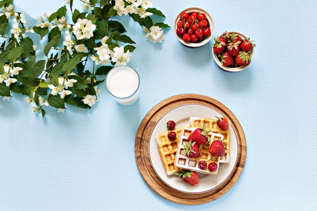 Prima colazione. Cialde viennesi con fragole e ciliegie su una tavola di legno. Primavera