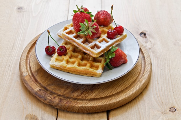 Prima colazione. Cialde viennesi con fragole e ciliegie su una tavola di legno. Primavera