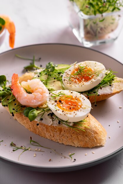 Prima colazione con bruschetta con gamberetti, uova e microgreens in un piatto, primi piani