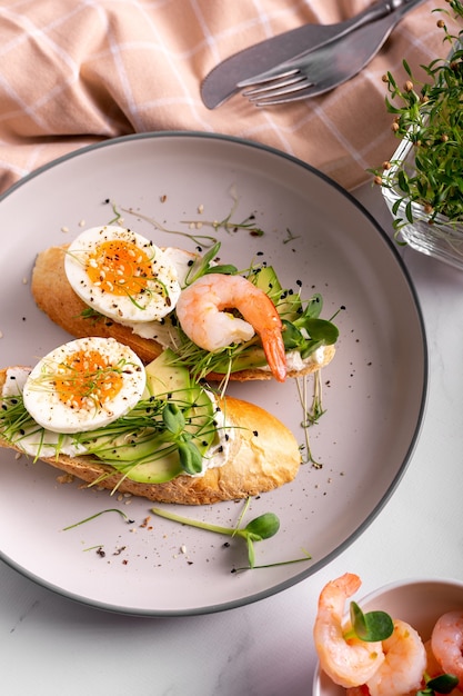 Prima colazione con bruschetta con gamberetti, uova e microgreens in un piatto, primi piani