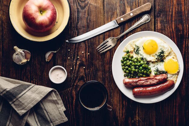 Prima colazione con uova fritte, salsicce e piselli sul piatto bianco