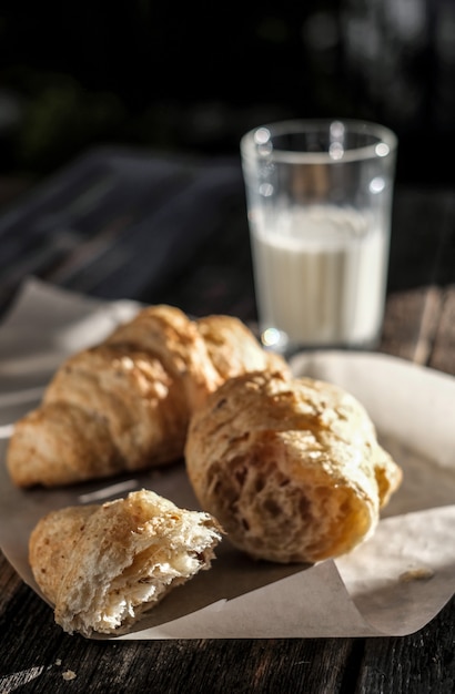 Prima colazione deliziosa con i croissant e il bicchiere di latte freschi sulla tavola di legno alla luce del sole