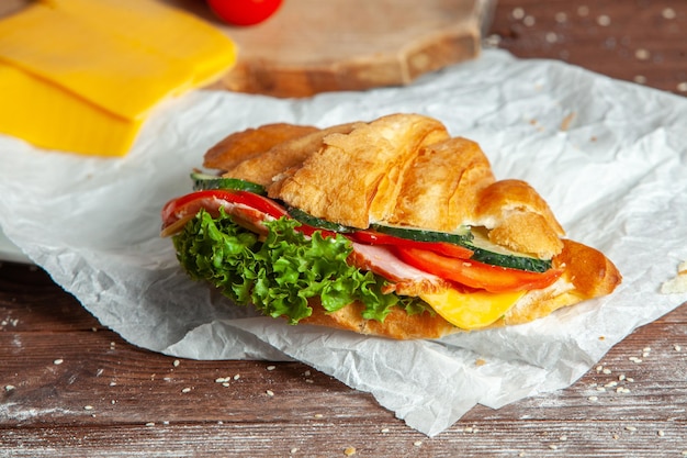 Prima colazione di croissant fresco con formaggio di prosciutto e foglia di insalata su fondo di legno bianco