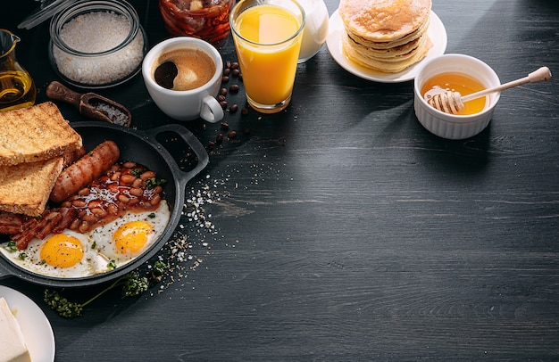 Prima colazione inglese su un tavolo scuro uova fritte con pancetta fagioli in scatola e salsiccia