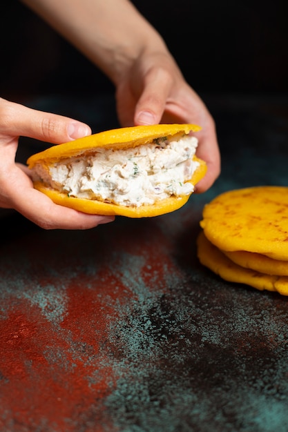 Prima colazione latinoamericana Arepas (arepa) di pasta di mais macinata con formaggio ed erbe. Le mani delle donne che tengono arepa. Cucina del Venezuela e della Colombia. Vista del primo piano, sfondo scuro, copia spazio. Verticale