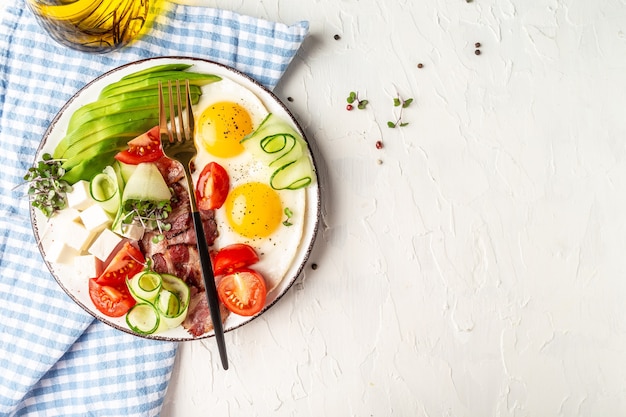 Prima colazione sana di dieta di cheto: uovo, avocado, formaggio, pancetta affumicata e insalata fresca sulla zolla bianca