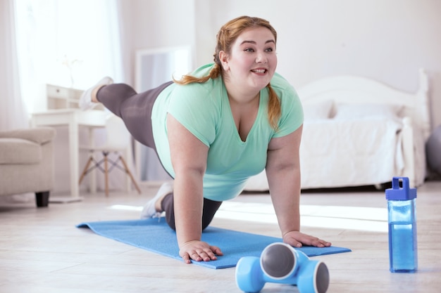 Prima lo stretching. Grassoccia giovane donna in piedi a quattro zampe mentre fa esercizi