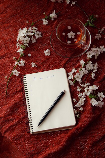 Primavera piatta vista dall'alto home office workspace - notebook con tazza da tè e rami di fiori di ciliegio su uno sfondo rosso della scrivania