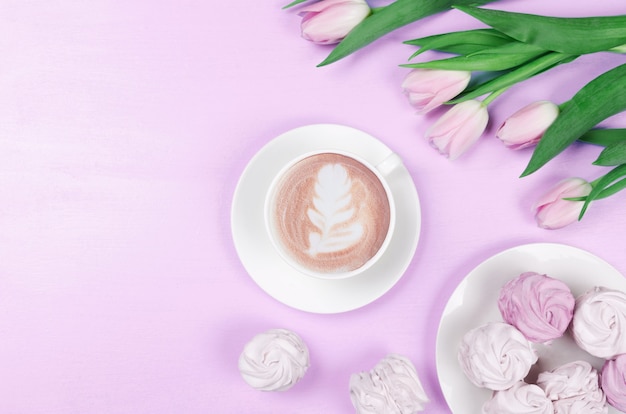 Primavera piatto lay. Tazza bianca con caffè, tulipani rosa e marshmallow. vista dall'alto, copia dello spazio