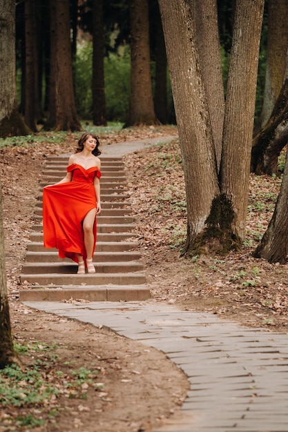 Primavera Ritratto di una ragazza che ride in un lungo abito rosso con i capelli lunghi, passeggiate nel parco nel bosco