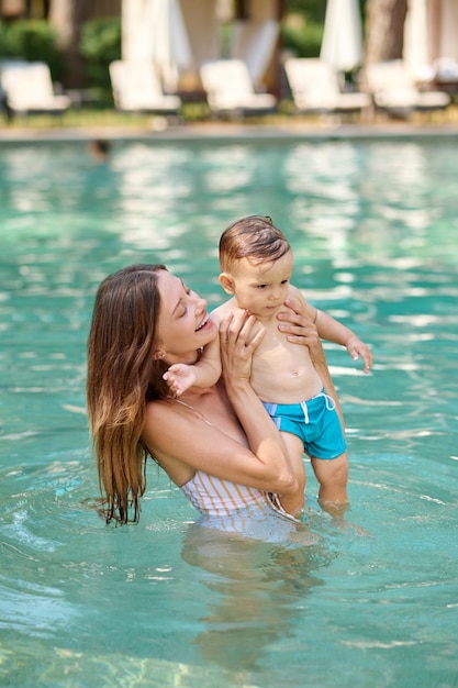 Primo bagno in piscina. Una giovane donna dai capelli lunghi che nuota in una piscina con il suo piccolo figlio