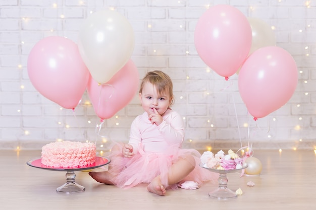 Primo compleanno bambina carina che mangia torta su sfondo muro di mattoni con luci e palloncini