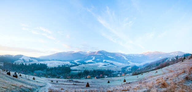 Primo gelo autunnale sul pascolo con mucchi di fieno e alba nel villaggio di montagna. Due colpi punto immagine.