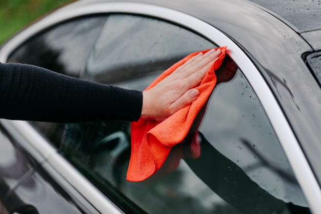 Primo piano a portata di mano con straccio pulizia finestrino laterale dell'auto nera