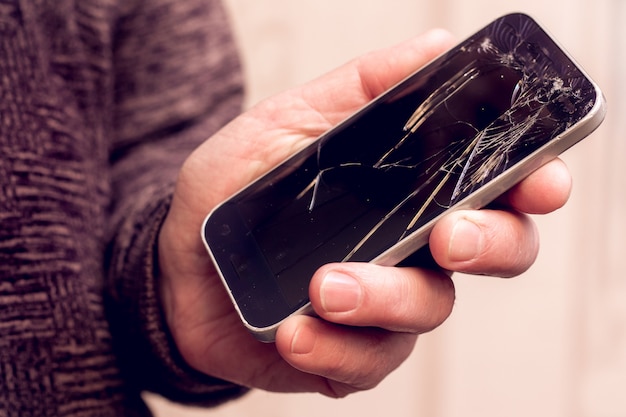 Primo piano a portata di mano in possesso di un telefono con vetri rotti