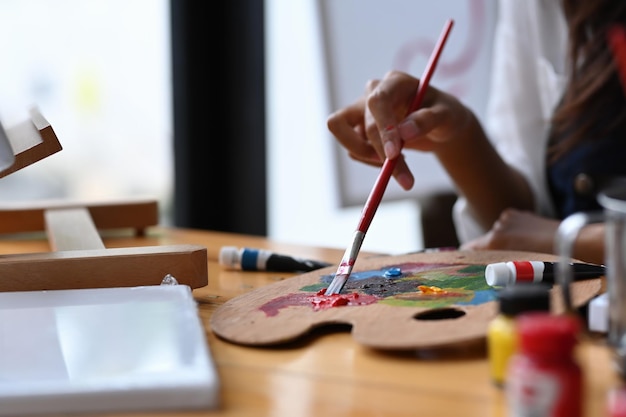 Primo piano artista femminile che tiene il pennello e mescola il colore sulla tavolozza