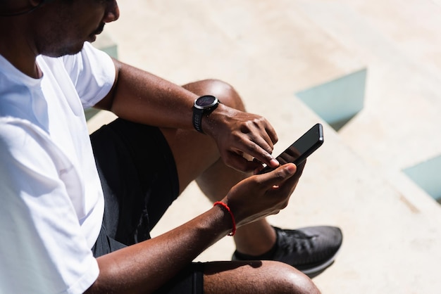 Primo piano asiatico giovane atleta sportivo corridore uomo nero indossa orologio intelligente dei tempi moderni e sincronizza con uno smartphone controlla il risultato in esecuzione dopo l'allenamento eseguito all'aperto, sana tecnologia di allenamento esercizio fisico