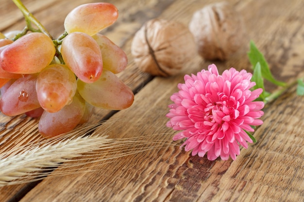 Primo piano aster rosso, uva e noci su vecchie tavole di legno. Profondità di campo. Scena autunnale.