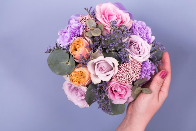 Primo piano bellissimi fiori in colori pastello su sfondo blu e mano di donne. Biglietto di auguri, festa della mamma, compleanno. Copia spazio.