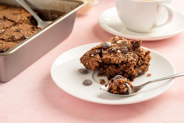 Primo piano brownies con scaglie di cioccolato e fiocchi d'avena serviti con una tazza di tè su sfondo rosa