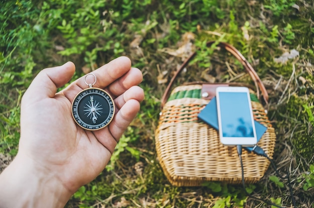 Primo piano, bussola nella mano di un ragazzo. sullo sfondo Powerbank con uno smartphone su un cesto nella foresta.