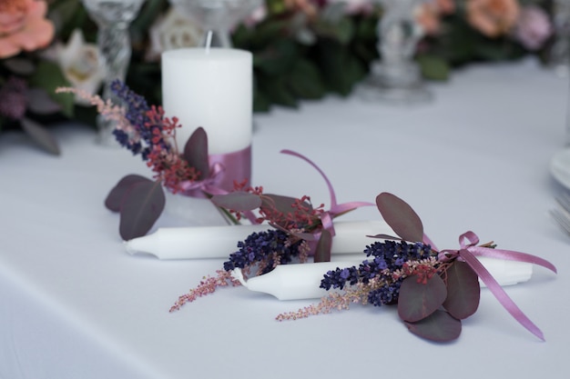 Primo piano candela decorata con rami di eucalipto, astilbe e lavanda freschi legati con nastro rosa.