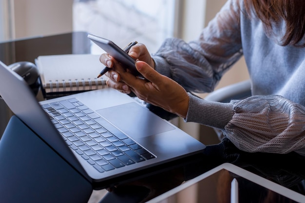 Primo piano casual donna d'affari mano utilizzando smartphone mobile e lavorare sul computer portatile sul posto di lavoro